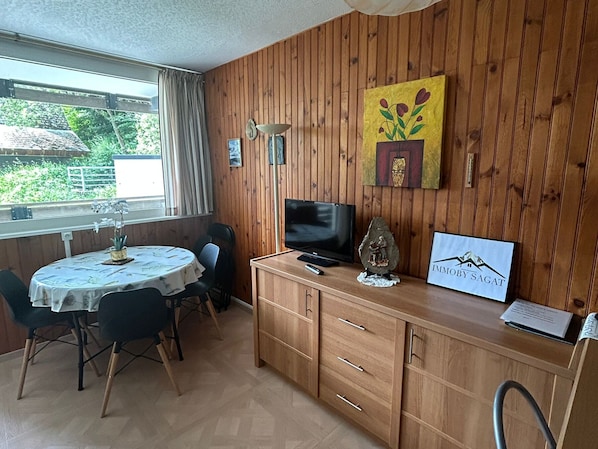 A wooden-paneled room with a dining table, chairs, a TV, a decorative stone, and a framed picture. - Cozy 1-bedroom apartment in Super Besse center (Besse-et-Saint-Anastaise-Super Besse)