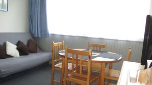 A room with a grey sofa, wooden chairs, a small table, and a TV.