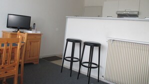 A small kitchenette with a microwave, a coffee maker, and a toaster. There are two wooden chairs and a small table with a television.