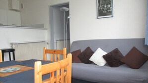 A living room with a grey sofa, wooden chairs, a table with a placemat, a floor lamp, and a framed picture on the wall.