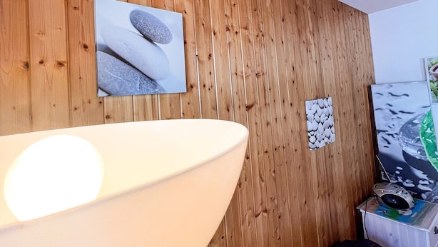 A room with a wooden wall, a large white bathtub, and a television on a stand.
