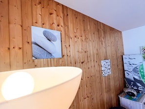 A room with a wooden wall, a large white bathtub, and a television on a stand.