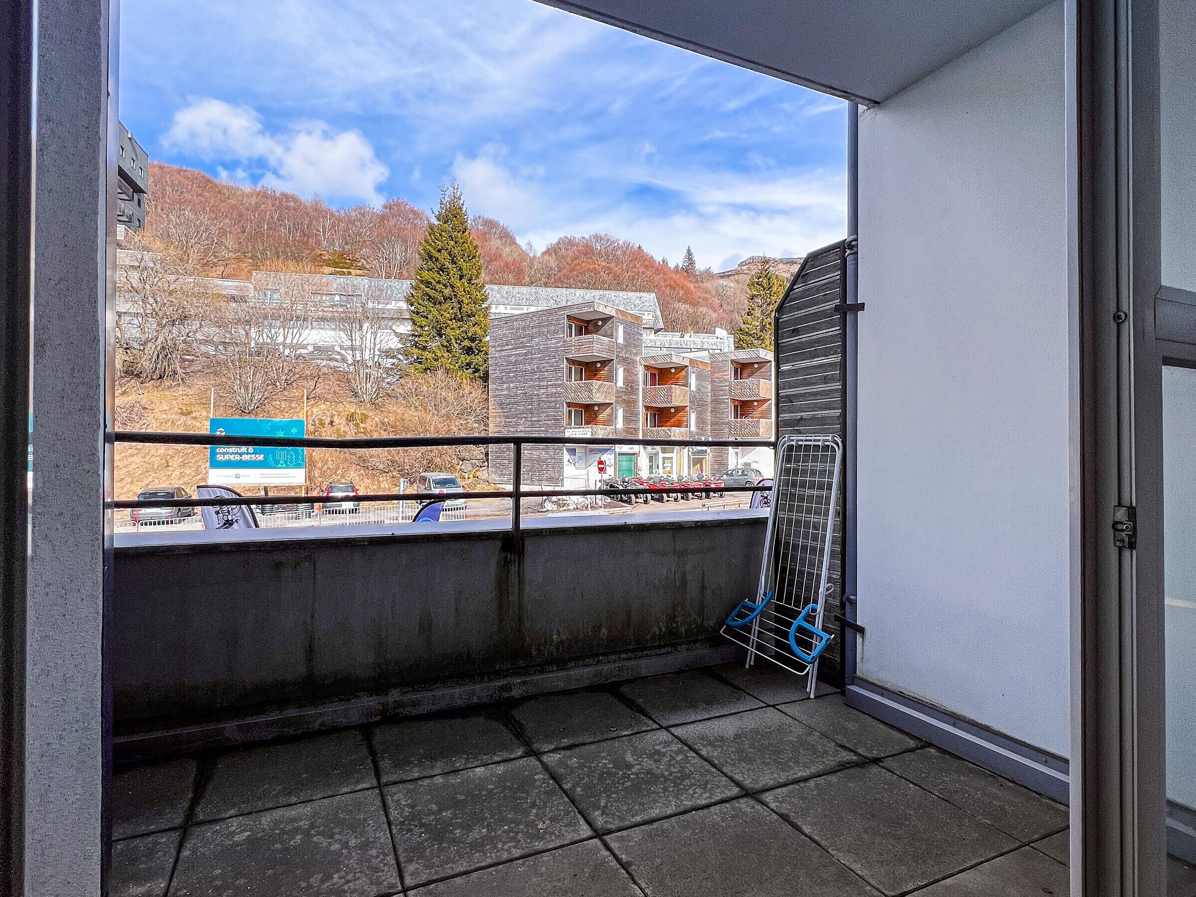A balcony with a view of a building with multiple balconies, a signboard, and parked cars.