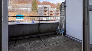 A balcony with a view of a building with multiple balconies, a signboard, and parked cars.