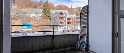 A balcony with a view of a building with multiple balconies, a signboard, and parked cars.