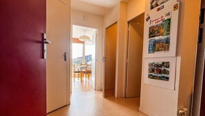 Un couloir avec une porte rouge, un coin repas avec une table et des chaises, et un mur orné de divers affiches.