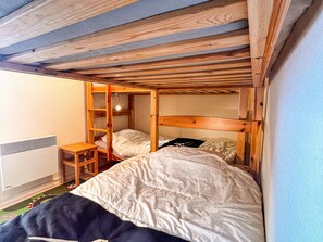 Une chambre avec un lit superposé, des poutres en bois, une petite table en bois et un radiateur.