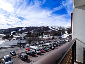 Un parking avec des voitures et un fourgon, d’où l’on peut admirer un paysage montagneux enneigé.