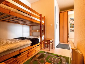 Een slaapkamer met een stapelbed, een klein bureau en stoel, een deur, en een muur met afbeeldingen.