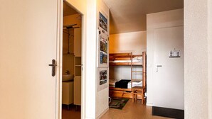 Un couloir étroit avec un lit superposé, une petite salle de bain et une porte sur laquelle est apposée une pancarte.
