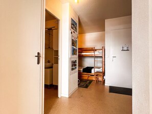 Un couloir étroit avec un lit superposé, une petite salle de bain et une porte sur laquelle est apposée une pancarte.