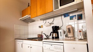 Une cuisine compacte dotée de meubles blancs, d’un four à micro-ondes, d’une machine à café et d’un lave-vaisselle.