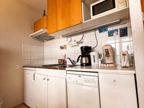 A compact kitchen with white cabinets, a microwave, a coffee maker, and a dishwasher.