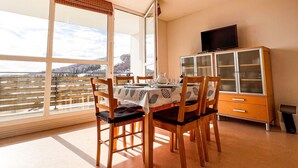 Un coin repas avec une table dressée pour quatre personnes, des chaises en bois, un buffet aux portes vitrées et une vue sur un paysage enneigé par de grandes fenêtres.