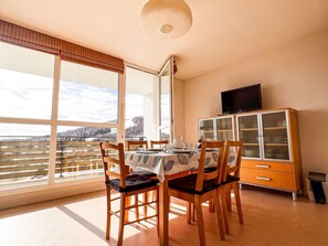 A dining area with a table set for four, wooden chairs, a cabinet with glass doors, and a view of a snowy landscape through large windows.