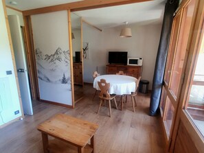 Een eethoek met een houten tafel en stoelen, een televisie op een kast, en een schuifdeur met een berglandschap.