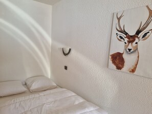 A bedroom with a bed, a white textured wall, a painting of a deer, and a wall-mounted light fixture.