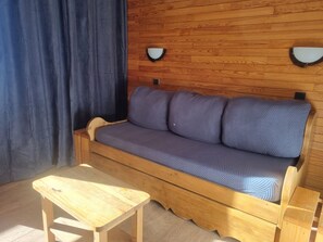 Un sofá de madera con un cojín de estampado en espiga, un muro de madera, una pequeña mesa de madera y dos lámparas fijadas a la pared.