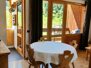 A wooden dining area with a round table and chairs, a wooden door, and a view of a forested landscape.