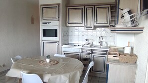 A compact kitchen with a dining table, chairs, a small potted plant, and a white fan on a shelf. - Cozy F3 apartment near slopes, perfect for families (Besse-et-Saint-Anastaise-Super Besse)