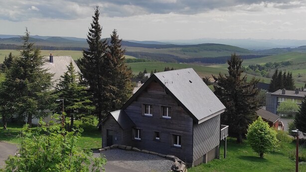 A house with a sloped roof, surrounded by trees and a view of distant hills. - Cozy F3 apartment near slopes, perfect for families (Besse-et-Saint-Anastaise-Super Besse)