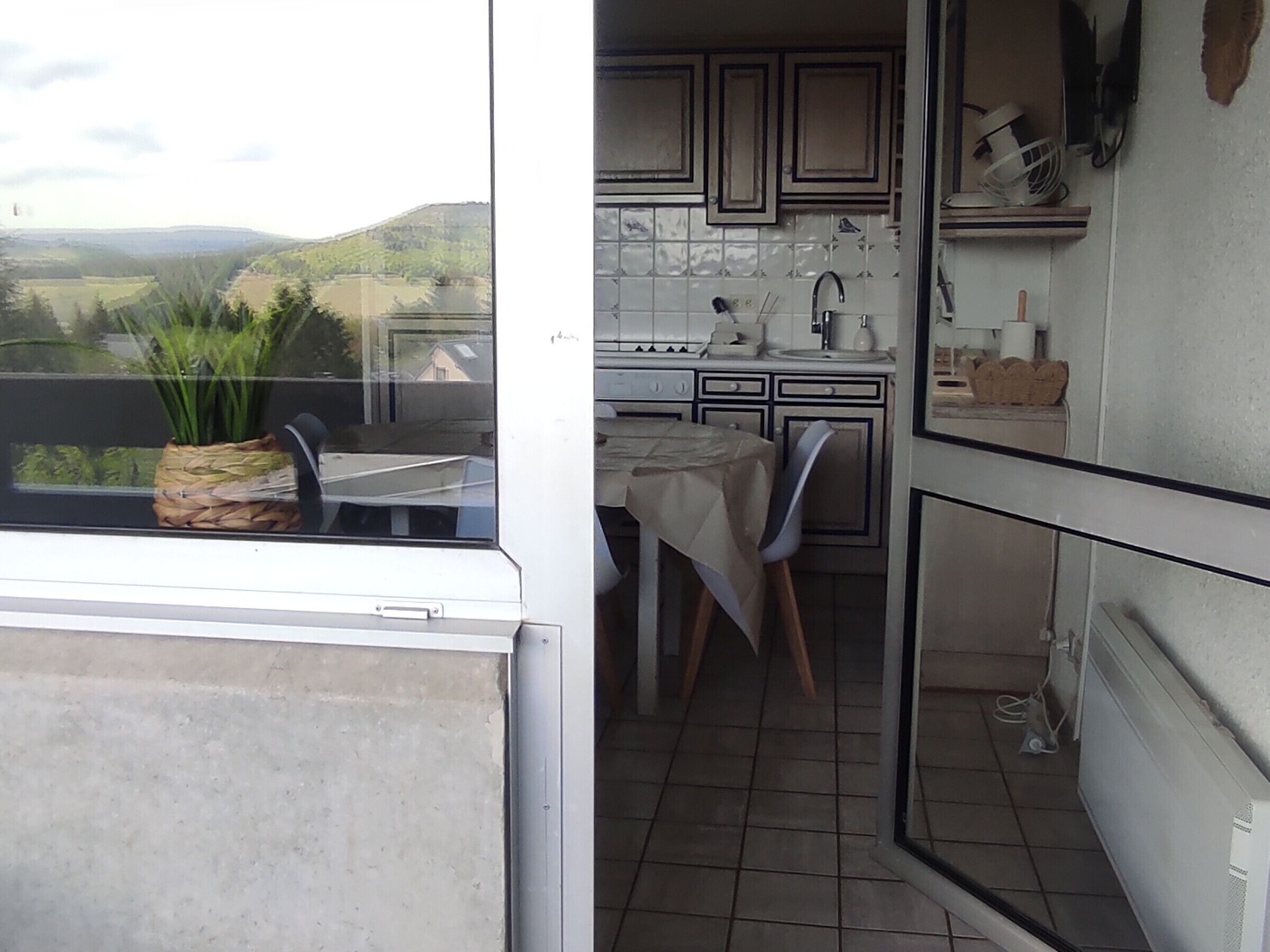 A small kitchen with a window overlooking a scenic view, a table with chairs, and a potted plant.
