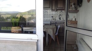 A small kitchen with a window overlooking a scenic view, a table with chairs, and a potted plant. - Cozy F3 apartment near slopes, perfect for families (Besse-et-Saint-Anastaise-Super Besse)