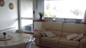 A living room with a beige sofa, a dining table with a white tablecloth, and a potted plant on a small table. - Cozy F3 apartment near slopes, perfect for families (Besse-et-Saint-Anastaise-Super Besse)