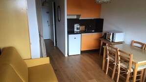 Ein kompakter Wohnraum mit Küchenzeile, einem Essbereich mit Holzmöbeln und einer Couch.