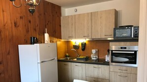 Een keuken met houten kastjes, een witte koelkast, een magnetron, een koffiezetapparaat en een broodrooster.