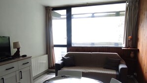 Een slaapkamer met een bed, een televisie, een bureau en een raam met gordijnen.