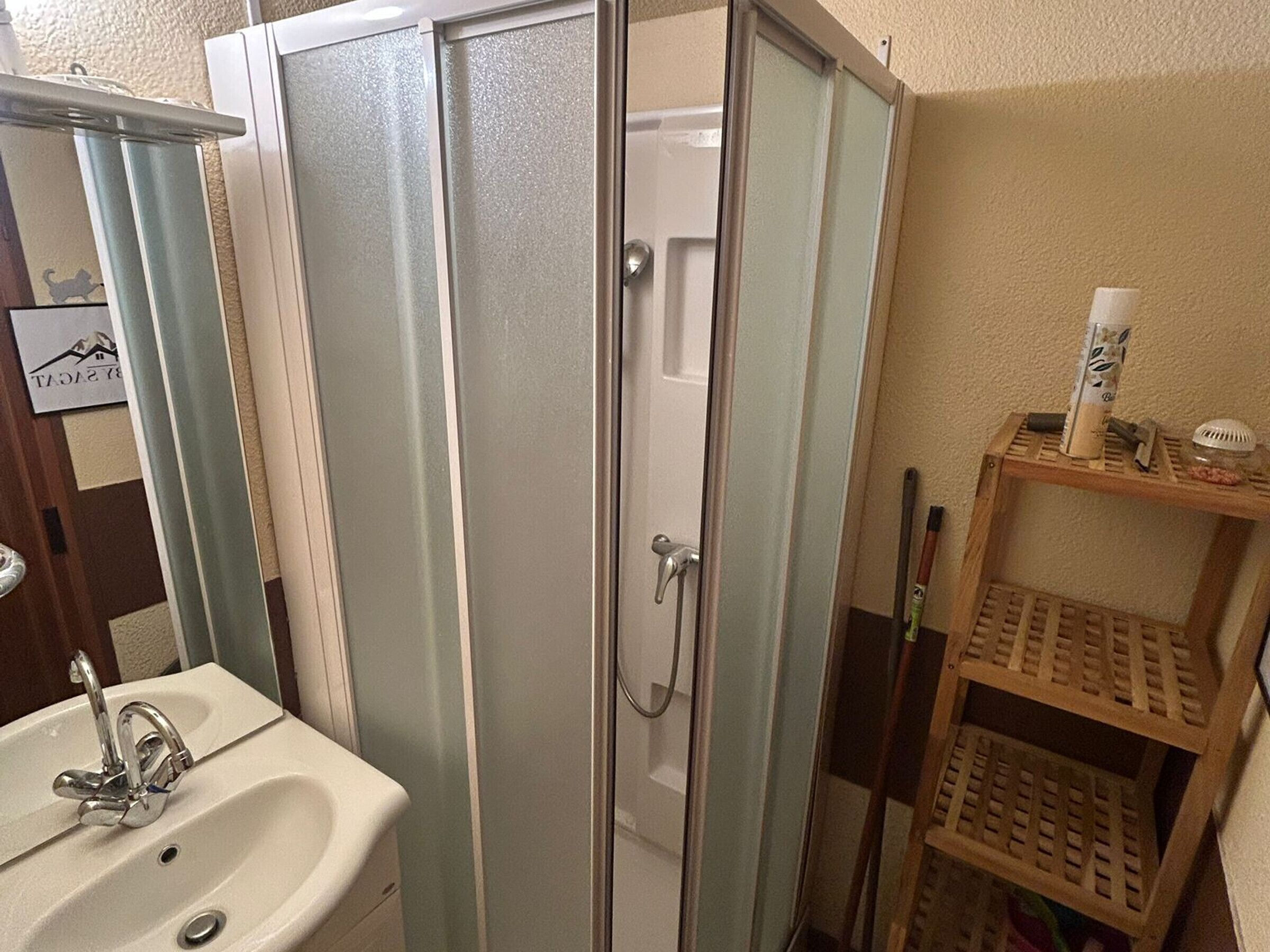 A bathroom with a sink, a glass shower enclosure, and a wooden shelf with toiletries.