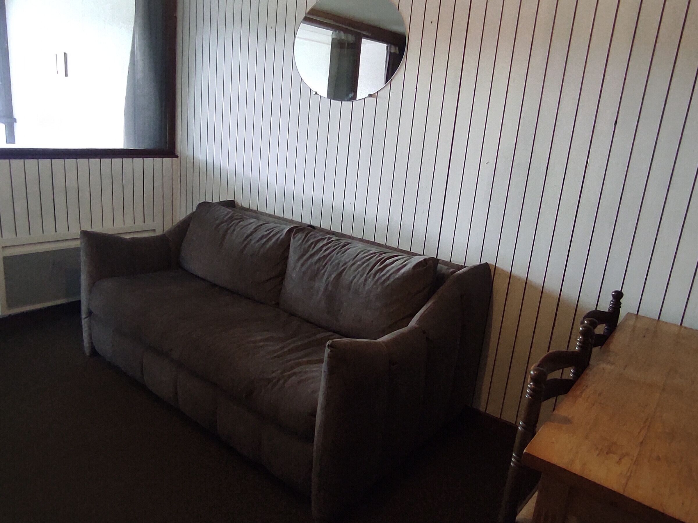 A room with a brown sofa, a wooden table, and a wall-mounted mirror.