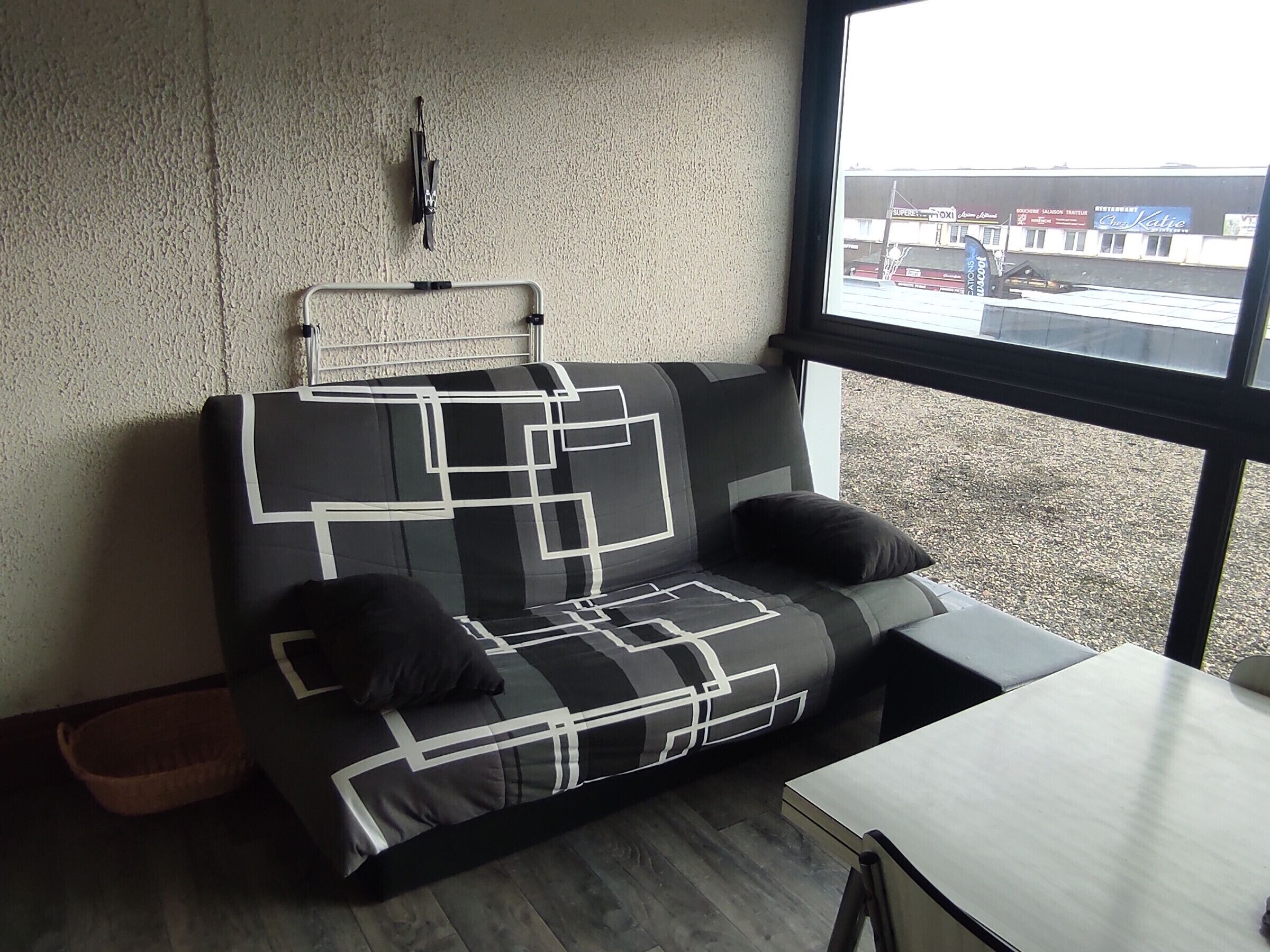A modern room with a black and white patterned sofa, a small table, and a window with a view of a building and a parking lot.