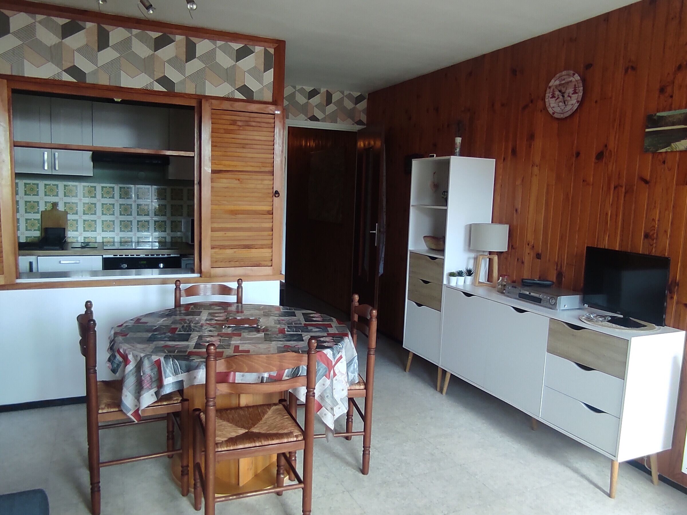 Cozinha compacta com mesa de jantar, cadeiras, armário com porta de madeira e televisão em um móvel.