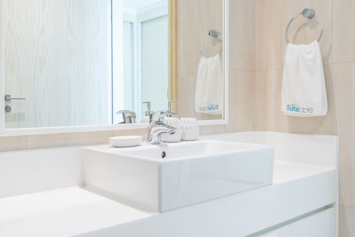 Ein modernes Badezimmer mit einem großen, weißen Waschbecken, einem Spiegel und zwei Handtüchern, die an Handtuchhaken hängen.