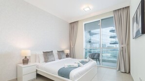 Moderni hotellihuone, jossa on suuri sänky, kaksi yöpöytää, yölamppu, ikkuna verhoilla ja näkymä kaupunkimaisemaan.