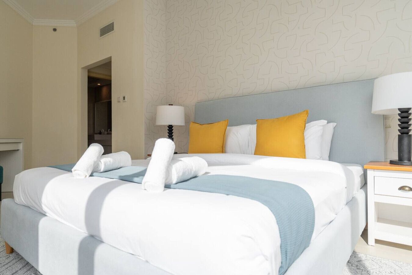 Ein Hotelzimmer mit einem großen Bett, zwei Nachttischen, einem Beistelltisch und einer Tür zu einem Badezimmer.