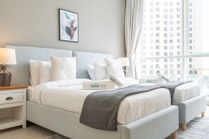 A hotel room with a bed, bedside tables, a lamp, a window with a view of buildings, and a framed picture on the wall.