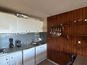 Une cuisine de taille réduite avec des meubles blancs, un évier encastré et un mur en bois.