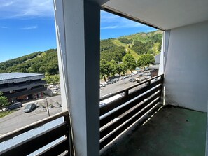 Un balcon donnant sur une route, un immeuble et un paysage vallonné.