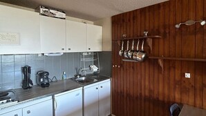 A compact kitchen with white cabinets, a built-in sink, and a wooden wall. - Central apartment, access to slopes, south balcony, WIFI, nearby parking (Besse-et-Saint-Anastaise-Super Besse)