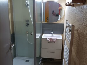 Une salle de bain avec une douche à parois de verre, un lavabo blanc avec une serviette et un miroir.