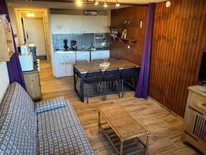 A compact living space with a sofa, a dining table with chairs, a small kitchen area, and a television.