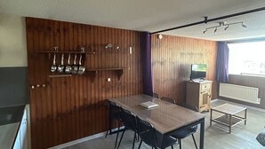 A compact kitchen with wooden paneling, a dining table with chairs, a small TV, and a radiator. - Central apartment, access to slopes, south balcony, WIFI, nearby parking (Besse-et-Saint-Anastaise-Super Besse)