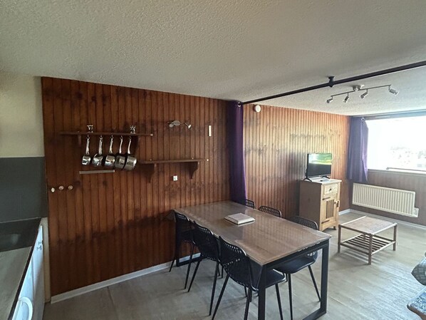 A compact kitchen with wooden paneling, a dining table with chairs, a small TV, and a radiator. - Central apartment, access to slopes, south balcony, WIFI, nearby parking (Besse-et-Saint-Anastaise-Super Besse)