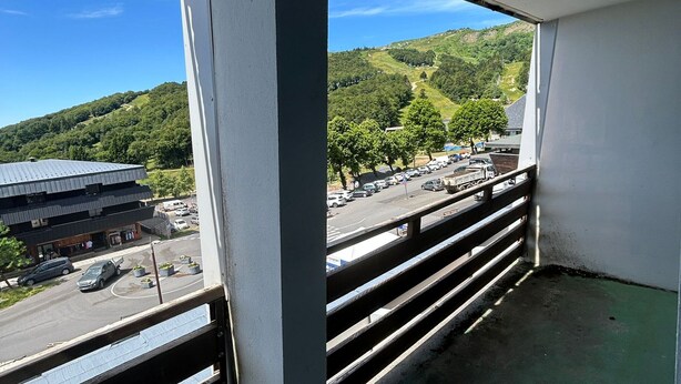 A balcony with a view of a road, a building, and a hilly landscape. - Central apartment, access to slopes, south balcony, WIFI, nearby parking (Besse-et-Saint-Anastaise-Super Besse)