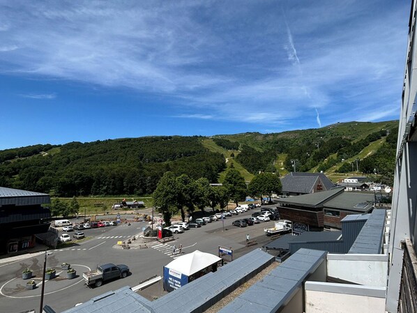Un parking rempli de véhicules, un bâtiment doté d’un toit plat et, au loin, un paysage vallonné.