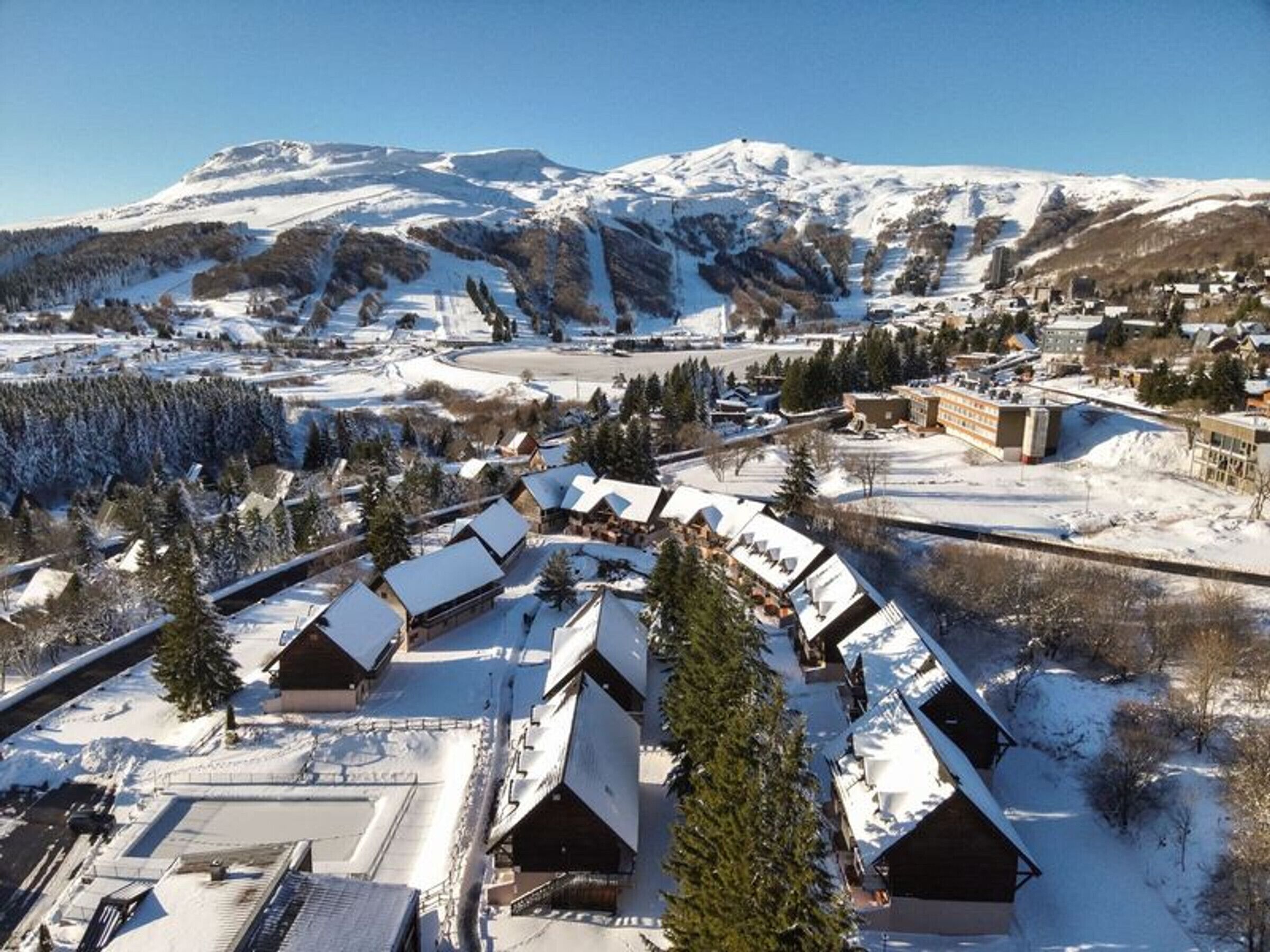 Un village enneigé, avec ses bâtiments traditionnels en bois, une piste de ski et des montagnes en arrière-plan.