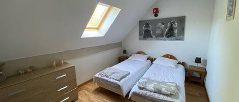 Quarto com duas camas, um claraboia, cómoda de madeira e um quadro na parede.